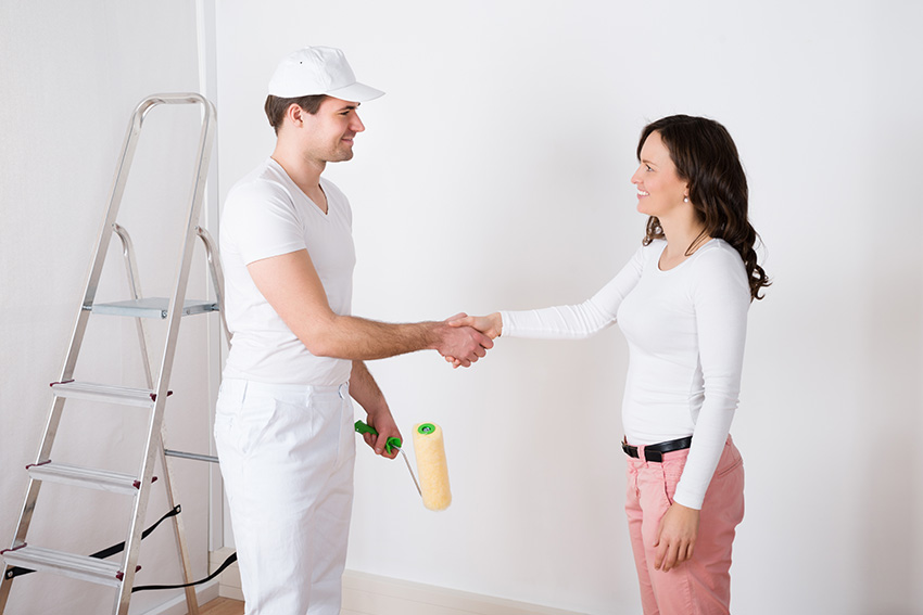 Young Beautiful Woman Shaking Hands To Painter With Paint Roller At Home