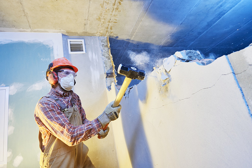 Worker builder with sledgehammer destroying interior wall